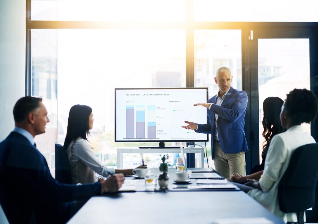 A business professional giving a sales pitch to a boardroom filled with clients